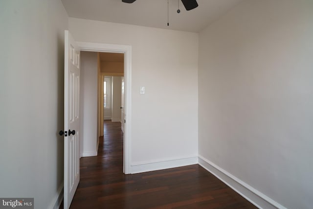 empty room featuring dark wood finished floors, a ceiling fan, and baseboards