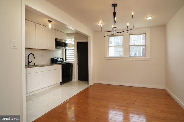 kitchen featuring a sink, white cabinetry, backsplash, stainless steel microwave, and gas stove