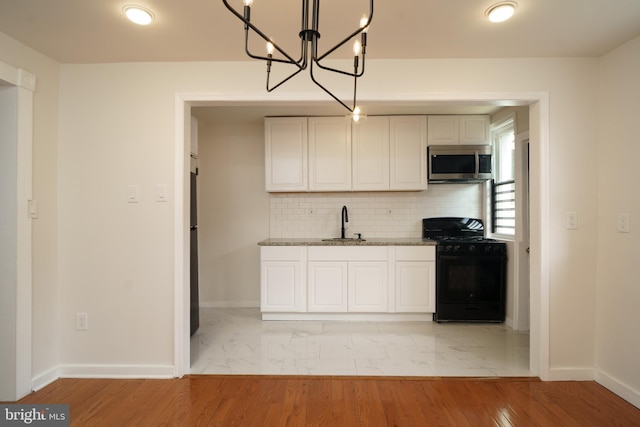 kitchen with decorative backsplash, stone countertops, a sink, black appliances, and baseboards