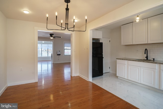 kitchen featuring tasteful backsplash, freestanding refrigerator, white cabinetry, a sink, and baseboards