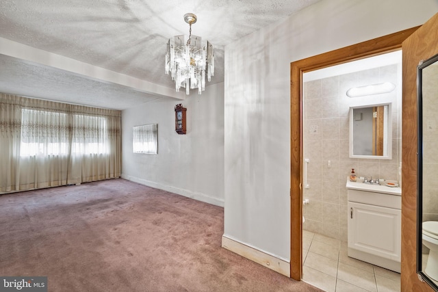 carpeted empty room featuring an inviting chandelier, sink, tile walls, and a textured ceiling