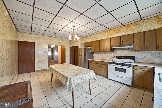 kitchen featuring stainless steel refrigerator, decorative light fixtures, light tile patterned floors, white range with gas stovetop, and an inviting chandelier