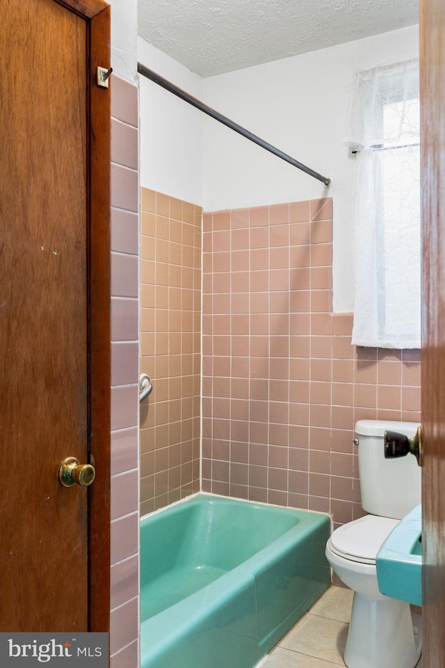 bathroom with shower / washtub combination, tile walls, tile patterned flooring, toilet, and a textured ceiling