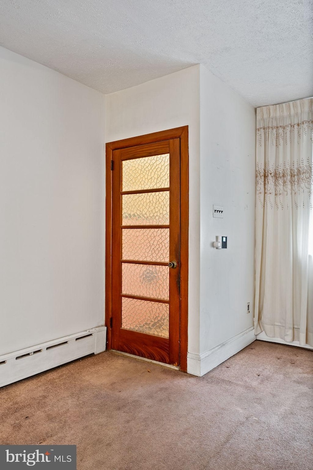 carpeted empty room featuring a baseboard heating unit and a textured ceiling