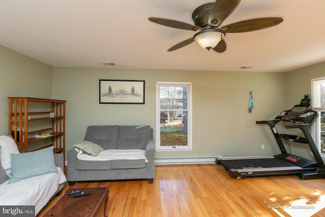 workout room featuring hardwood / wood-style floors, a wealth of natural light, ceiling fan, and a baseboard heating unit