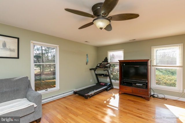 workout area with wood-type flooring, a wealth of natural light, ceiling fan, and baseboard heating