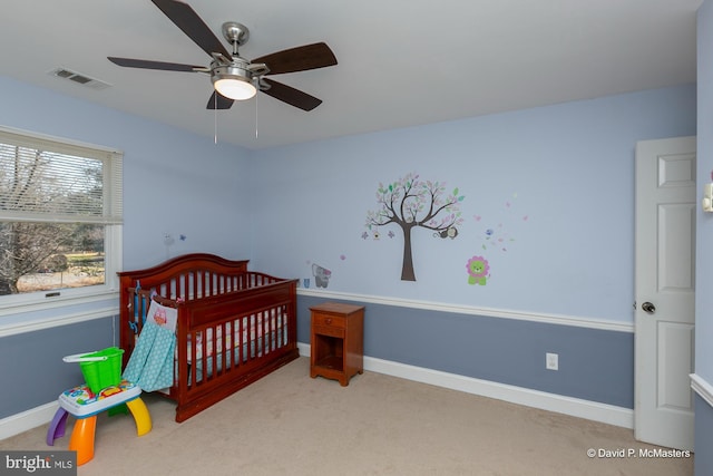 carpeted bedroom with a crib and ceiling fan