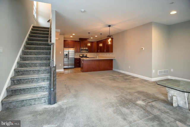 kitchen featuring stainless steel appliances, decorative light fixtures, a center island, and light carpet