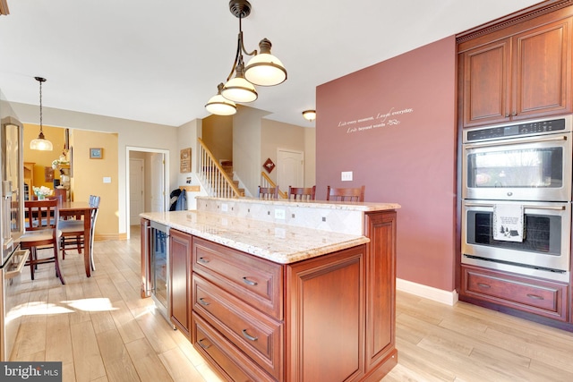 kitchen with a center island, hanging light fixtures, light wood-style flooring, stainless steel double oven, and light stone countertops