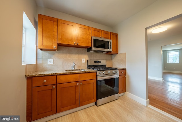 kitchen with tasteful backsplash, sink, light hardwood / wood-style flooring, and appliances with stainless steel finishes