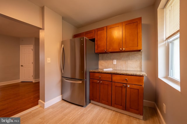 kitchen featuring tasteful backsplash, light stone counters, stainless steel refrigerator, and light hardwood / wood-style flooring