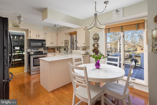 kitchen featuring black appliances, a peninsula, a sink, and light wood-style floors