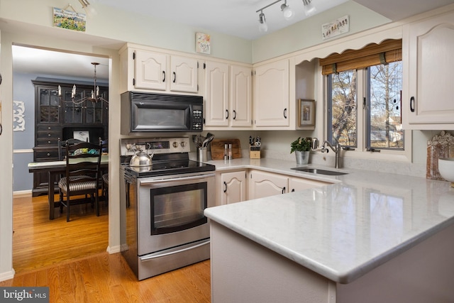 kitchen featuring black microwave, a peninsula, a sink, light wood-type flooring, and stainless steel electric stove