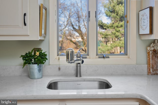 kitchen with light stone countertops, white cabinetry, and a sink