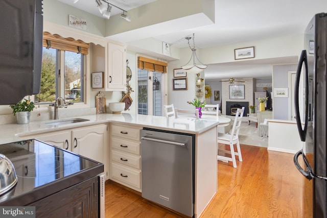 kitchen with light wood-style flooring, light countertops, black appliances, a fireplace, and a sink