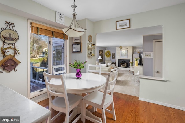 dining area with a brick fireplace, wood finished floors, a ceiling fan, and baseboards