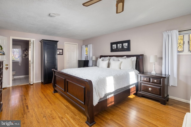 bedroom with a ceiling fan, connected bathroom, light wood-style flooring, and baseboards