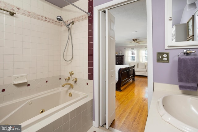 ensuite bathroom featuring a combined bath / shower with jetted tub, ceiling fan, vanity, ensuite bath, and wood finished floors