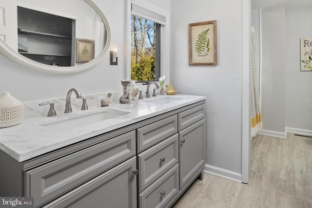 bathroom featuring double vanity, wood finished floors, a sink, and baseboards