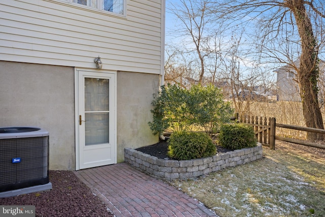 entrance to property featuring fence, central AC, and stucco siding