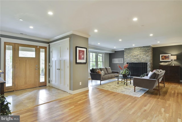 entrance foyer with ornamental molding, a stone fireplace, and light hardwood / wood-style floors