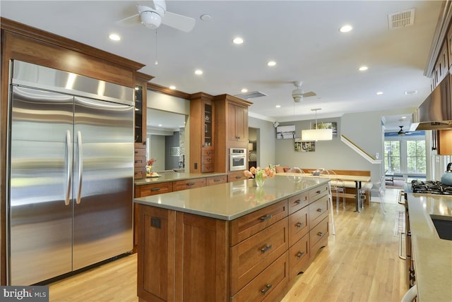 kitchen featuring light hardwood / wood-style flooring, ceiling fan, stainless steel appliances, a kitchen island, and decorative light fixtures