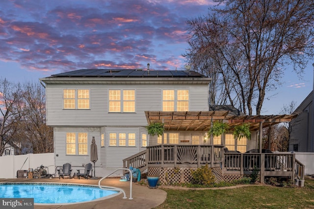 back of property at dusk with a fenced in pool, fence, a wooden deck, solar panels, and a pergola