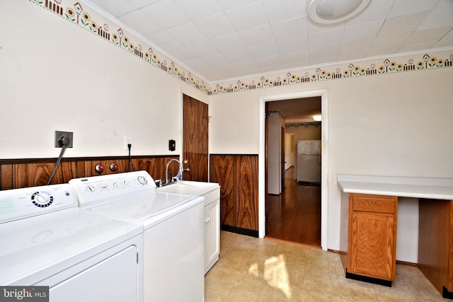 laundry area featuring wood walls, sink, cabinets, crown molding, and washer and clothes dryer