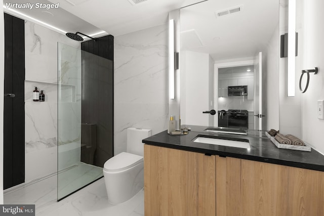 bathroom with vanity, tile walls, toilet, and tiled shower