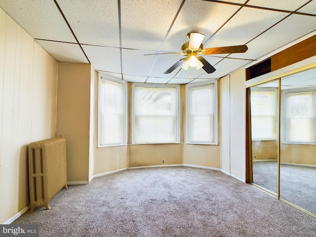 carpeted spare room featuring ceiling fan, a healthy amount of sunlight, radiator, and wood walls