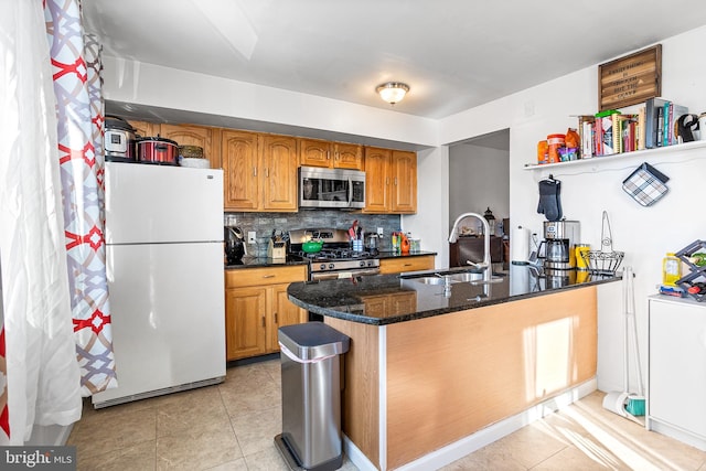 kitchen featuring decorative backsplash, dark stone counters, appliances with stainless steel finishes, brown cabinets, and a sink