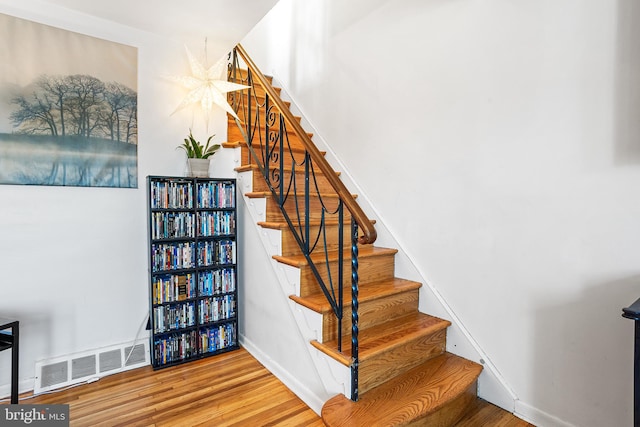 staircase with baseboards, visible vents, and wood finished floors