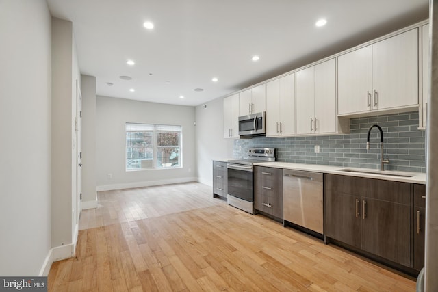 kitchen with sink, appliances with stainless steel finishes, dark brown cabinetry, tasteful backsplash, and light hardwood / wood-style floors