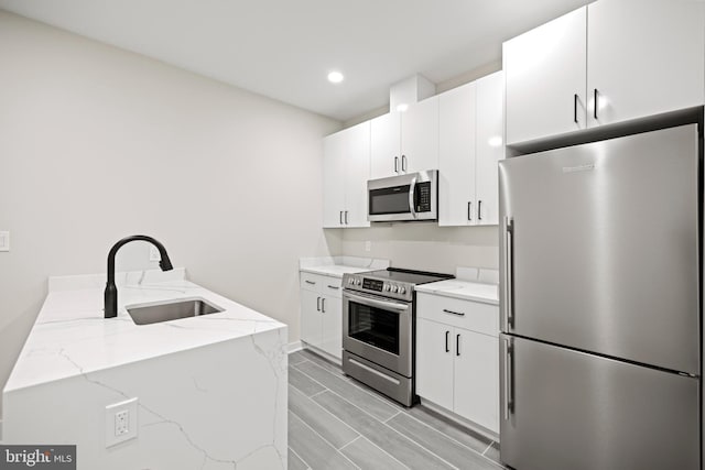 kitchen featuring light stone counters, sink, stainless steel appliances, and white cabinets