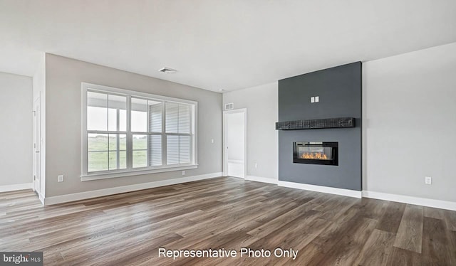 unfurnished living room with a large fireplace, baseboards, and wood finished floors