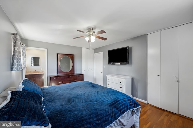 bedroom with a ceiling fan, wood finished floors, baseboards, ensuite bath, and two closets