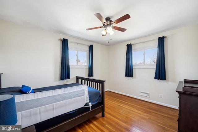 bedroom featuring a ceiling fan, multiple windows, wood finished floors, and baseboards