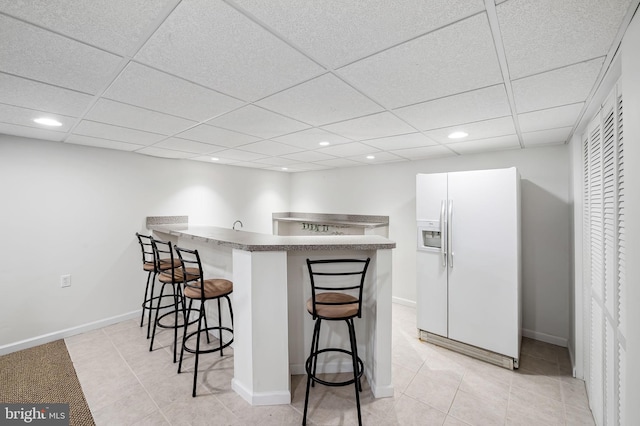 kitchen featuring light tile patterned floors, a kitchen bar, white refrigerator with ice dispenser, and a peninsula