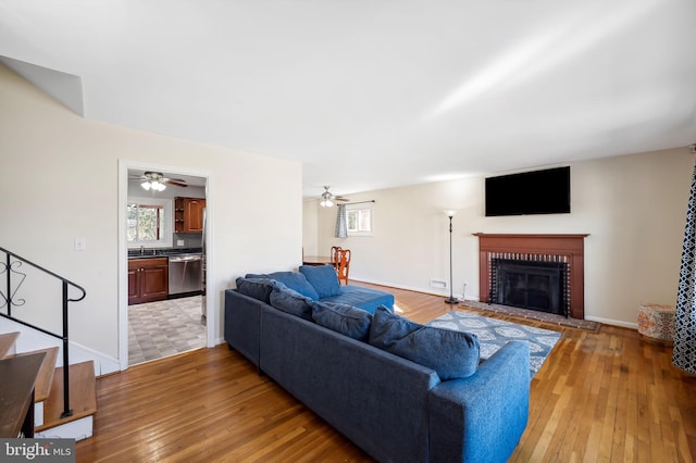 living area with stairway, a brick fireplace, baseboards, and light wood-style floors