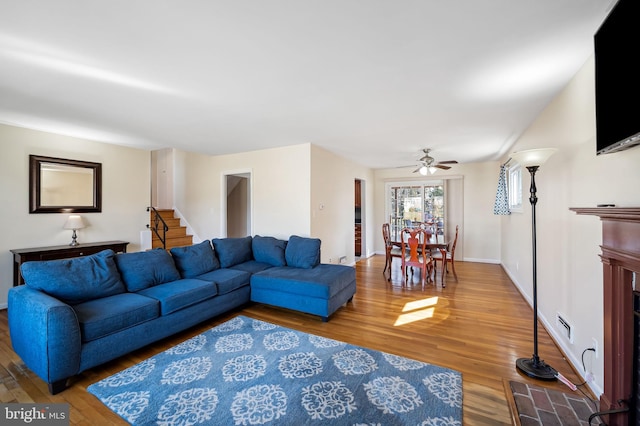 living room featuring stairway, a ceiling fan, wood finished floors, visible vents, and baseboards