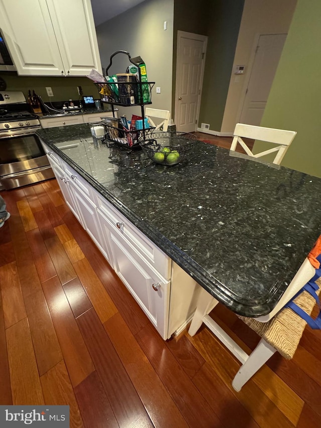 kitchen with dark wood-type flooring, dark stone countertops, a kitchen breakfast bar, stainless steel range with gas stovetop, and white cabinets