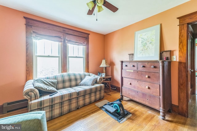 living area featuring a baseboard heating unit, a ceiling fan, and wood-type flooring