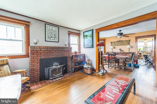 living area with hardwood / wood-style flooring, a ceiling fan, a healthy amount of sunlight, and a wood stove