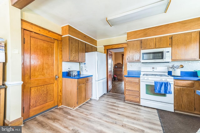 kitchen with brown cabinets, tasteful backsplash, light wood finished floors, and white appliances
