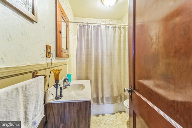bathroom featuring shower / tub combo with curtain, toilet, vanity, and wainscoting