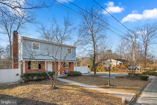 view of front of house featuring brick siding, a chimney, and fence