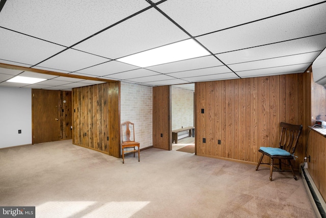 unfurnished room featuring light carpet, wood walls, baseboard heating, and a drop ceiling