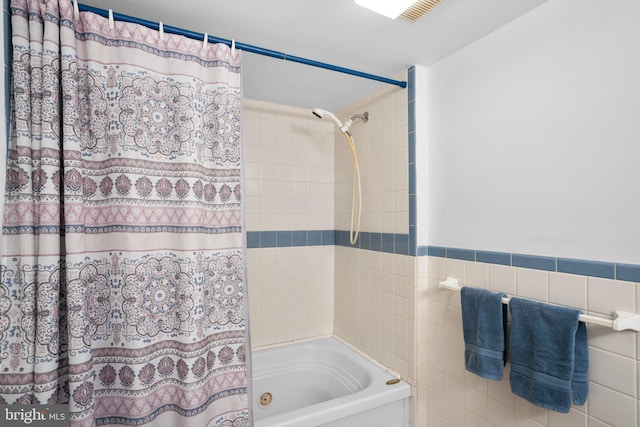 bathroom featuring a wainscoted wall, tile walls, and shower / bath combo with shower curtain