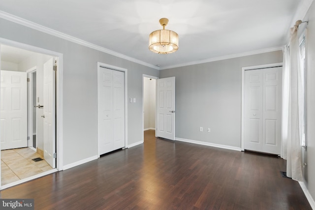 unfurnished bedroom featuring wood finished floors, baseboards, an inviting chandelier, crown molding, and two closets