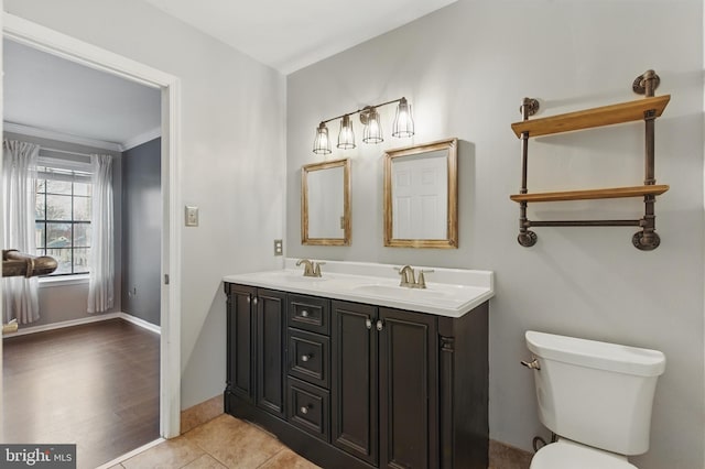 bathroom featuring baseboards, double vanity, a sink, tile patterned floors, and toilet